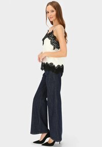 Biała koszulka na cienkich ramiączkach z czarną koronkową lamówką, zestawiona z ciemnymi szerokimi spodniami dżinsowymi i czarnymi szpilkami w szpic.