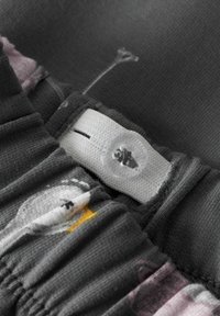 Izbliza elastična traka na tamnom materijalu s podesivim bijelim gumbom i elastičnom trakom, s otisnutim motivima ptica i cvjetova.