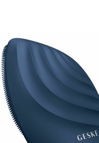 Marinblå hårborste med en vågig, ergonomisk design; har gummibelagda borst och en slät, matta yta. Varumärket "GESKE" präglat.