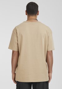Beige katoenen t-shirt met korte mouwen, losse pasvorm, ronde hals en een klein logo label op de zijnaad. Gladde textuur en eenvoudig ontwerp.