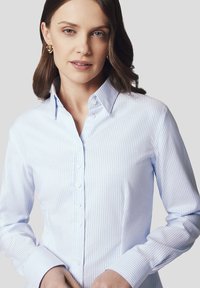 Jasnoniebieska i biała koszula z długim rękawem i kołnierzykiem w paski. Posiada gładką fakturę i klasyczny krój.