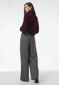 Bordeaux trui met opstaande kraag, gecombineerd met hoogwaardige, wijde grijze geruite broek, met een achterzak en een strakke uitstraling.