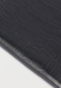 Sort læderartikel med præget krokodilleskinmønster og diskret præget mærkenavn på en hvid overflade.