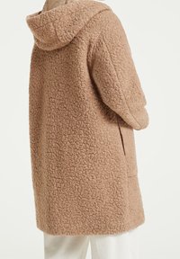 Abrigo largo con capucha en un tejido texturizado de color marrón claro con un aspecto esponjoso, que cuenta con bolsillos laterales y un ajuste holgado.