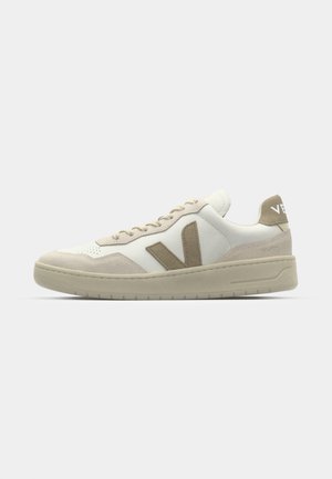 Beige och vit sneaker med en texturerad mocka- och läderfinish, prydd med en framträdande beige V-logotyp, platta skosnören och en vadderad sula.