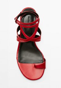 Sandale en cuir rouge avec des brides croisées, bout ouvert et semelle intérieure noire. Dispose d'une lanière à la cheville avec une boucle métallique en accent.