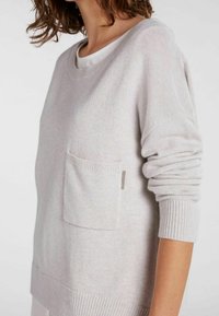 Hellgrauer Strickpullover mit gerippten Bündchen und Saum, ausgestattet mit einer vorderen aufgesetzten Tasche und einem abgerundeten Ausschnitt. Weiche Textur und lässige Passform.