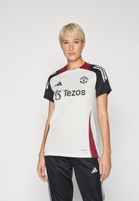 Balta futbolo marškiniai su juodomis rankovėmis ir bordo detalėmis. Yra apvalus iškirpimas, logotipas ir rėmėjo tekstas. Nešiojami su juodomis sportinėmis kelnėmis.