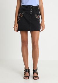 Svart denimkjol med frontknäppning och två fickor; har färgglada broderade mönster framtill.