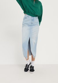 Falda de mezclilla azul claro con una abertura delantera, dobladillo deshilachado, diseño de cintura alta, combinada con zapatillas negras y calcetines blancos. Top verde corto.