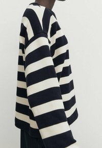 Tummansininen ja kerma valkoinen raidoitettu neulepusero pitkillä hihoilla, pyöreä pääntie ja ribbi rakenne. Raidat ovat leveät ja tasaisesti väliin jaettu.