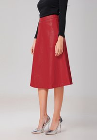 Jupe en cuir rouge en A avec une texture lisse, longueur mi-mollet et taille ajustée, associée à des talons aiguilles en argent brillant.