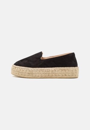 Sort ruskind slip-on espadrille med tyk flettet jutesål med plateau, set fra siden mod en hvid baggrund.