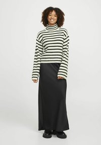 Pull rayé crème et noir, avec un col montant et des manches larges. Associé à une jupe maxi noire unie et des chaussures noires épaisses.