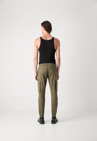 Top negro sin mangas, pantalones cargo oliva con cintura elástica, bolsillos laterales y puños ajustados. Tejido suave y diseño aerodinámico. Zapatos negros.