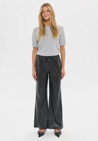 Top gris de manga corta, pantalones anchos de imitación cuero negro y zapatos negros de punta con detalles decorativos, estilizados para un look casual.