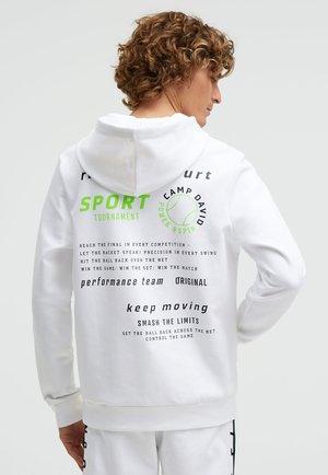 Person with curly hair wearing white hoodie featuring green and black sports-themed text and tennis ball graphic on the back.