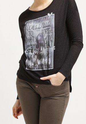 Schwarzes Langarmshirt mit zentralem Grafikdruck in weißem und grauem Schriftzug. Kombiniert mit olivgrünen, figurbetonten Hosen.