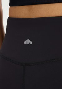 Zwarte hoge taille legging met een gladde textuur, een strakke pasvorm en een klein grijs logo boven de taille.