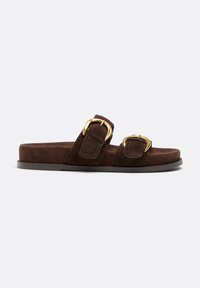 Sandale mule en daim marron avec deux larges brides ornées de grandes boucles dorées et une semelle plate noire.