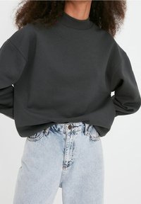 Sudadera gris oscuro con un cuello alto y hombros caídos. Combinada con unos pantalones vaqueros de tiro alto en azul claro, que muestran un corte holgado.