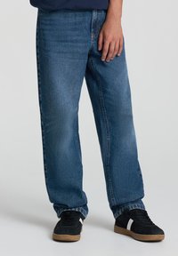 Jasnoniebieskie dżinsy o prostym kroju, wykonane z denimu, z kontrastowymi szwami, szlufkami na pasek oraz pięcioma kieszeniami. Noszone z czarnymi trampkami.