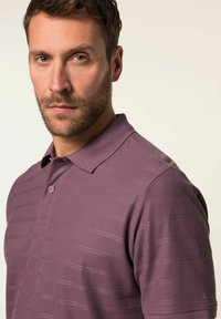 Polo à manches courtes de couleur violet foncé avec un motif texturé, deux boutons au col et un logo sur la manche inférieure.