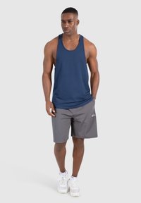 Canottiera blu navy abbinata a pantaloni corti grigi. La canottiera presenta un design classico, mentre i pantaloni corti hanno un piccolo logo sul lato. Sneakers bianche.