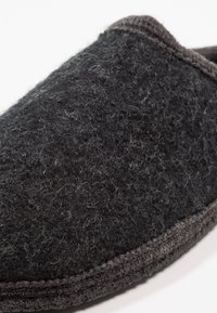 Zwarte vilten slipper met een gestructureerd oppervlak, afgeronde vorm en grijze accenten langs de rand. Zacht materiaal met zichtbare vezels.