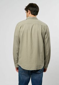 Camisa de manga larga verde clara con cuello, detalles de botones en los puños y un dobladillo ligeramente curvado, combinada con jeans azules.