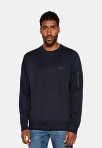 Felpa navy in cotone morbido con scollatura a girocollo a costine, maniche lunghe e tasca con zip sul braccio sinistro. Dettaglio logo discreto sul petto.