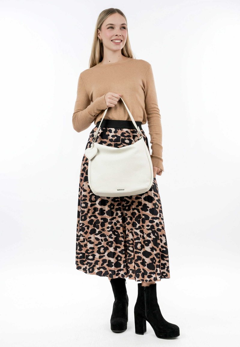 Weiße Leder-Schultertasche mit glatter Textur und einem herzförmigen Anhänger. Kombiniert mit einem plissierten Rock im Leopardenmuster und schwarzen Wildlederschuhen mit Absatz.