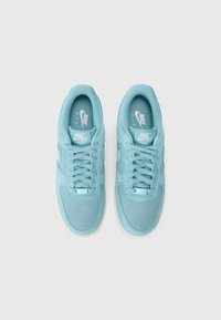 Világoskék Nike Air Force sneaker, sima velúr felülettel, perforált lábujjrésszel és azonos színű cipőfűzőkkel. Fehér logó a nyelvén és az oldalán.