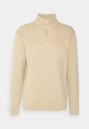 Beige sweater met ritssluiting en geribbelde textuur, lange mouwen en een hoge kraag. Beschikt over een halve rits aan de voorkant en zijsplitten in de zoom.