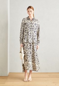 Srajca z dolgimi rokavi in maxi krilo v mornarsko modri in kremni paisley vzorcu, izdelano iz lahkotnega materiala. Ima majhno kremno torbico na rami.