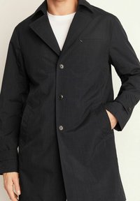 Svart, midjelång kappa av texturerat tyg med slagkrage, knappstängning, bröstficka och sidfickor.