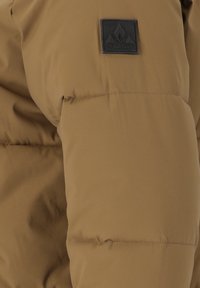 Bruine pufferjack met een gladde textuur, voorzien van een rechthoekig zwart label met een logo op de bovenste linkerarm.