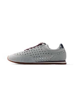 Zapatilla deportiva de ante gris con laterales perforados, cordones gris oscuro, acento metálico en el talón y suela de goma marrón vista de perfil.
