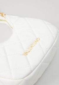 Weißer, gesteppter Sack aus synthetischem Material, mit einem goldenen "Valentino"-Logo und Reißverschlussdetail. Glatte Textur mit gepolsterter Optik.