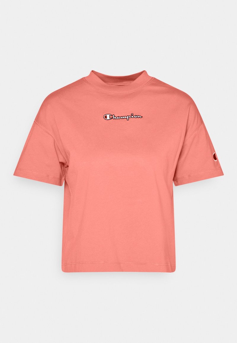 T-shirt court Champion rose corail avec manches courtes et logo brodé sur la poitrine et la manche gauche.