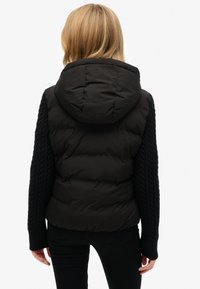 Zwarte donzen jas met capuchon, voorzien van kabelgebreide mouwen, een licht ingekort ontwerp en een gestructureerde afwerking op de mouwen.