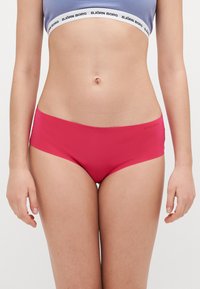 Slip da bagno rosso realizzato in tessuto liscio con design senza cuciture. Presenta un taglio a vita bassa e un logo discreto sul lato.