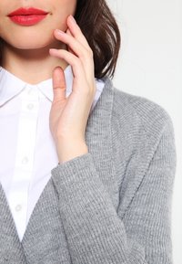 Harmaa neuletakki, joka on tehty ribbineuloksesta, yhdistettynä valkoiseen kauluspaitaan. Kuvassa näkyy pääntie ja osa hihoista.