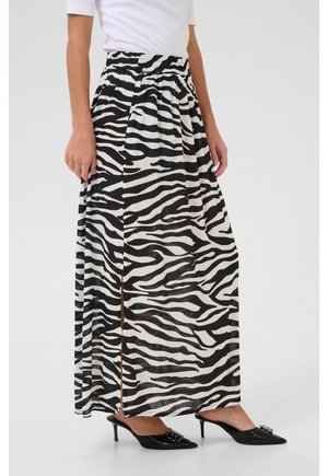 Donna con indosso una gonna lunga a stampa zebra bianca e nera con spacco laterale, top bianco e mules nere con tacco e punta affusolata.