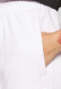 Ljust rosa sweatpants med elastisk midja och sidofickor, med en texturerad tyg och en vit logotypdetalj längst ner.