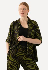 Black shirt with green and dark brown striped pattern, relaxed fit, short sleeves, open front, paired with matching patterned pants.