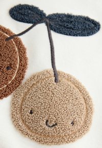 Design z texturované plyšové látky zobrazující béžový kulatý tvar s úsměvem, doplněný tmavě modrým listem a hnědými akcenty.