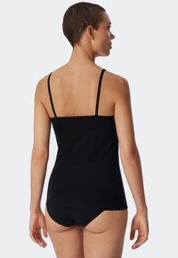 Zwarte katoenen tanktop met smalle bandjes, aansluitend ontwerp en een gladde textuur, gedragen met bijpassend zwart ondergoed tegen een neutrale achtergrond.