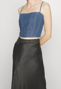 Ohutolkaiminen denimcroptoppi, jossa pystysuorat tikkaukset; yhdistetty mustaan satiinihameeseen, jossa on epäsymmetrinen helma ja merkitty vyötärönauha.