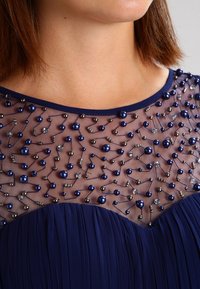 Close-up of a navy blue dress with sheer neckline decorated with dark blue and silver beads arranged in a connected pattern.